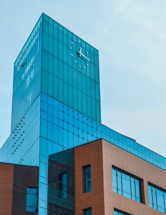 Low-angle view of a modern skyscraper with a glass facade featuring a prominent clock against a clear sky.